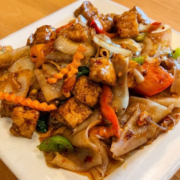 Close-up of a plate of Pad See Ew with tofu, wide noodles, and vegetables.